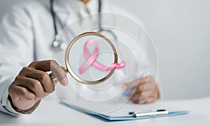 Doctor holding magnifier focus to virtual pink ribbon cancer, Breast cancer awareness
