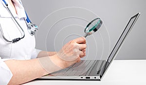 Doctor holding magnifier over laptop screen. Online medical consultation and checkup concept. Thorough analysis of