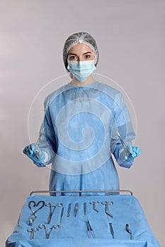 Doctor holding medical clamps near table with different surgical instruments on light background