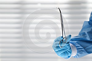 Doctor holding needle with suture thread indoors, closeup and space for text. Medical equipment