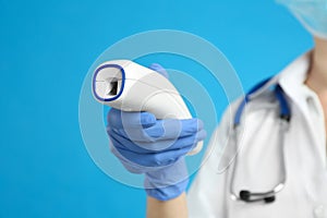 Doctor holding non contact infrared thermometer against blue background, focus on hand. Measuring temperature