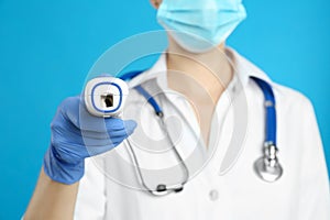 Doctor holding non contact infrared thermometer against blue background, focus on hand. Measuring temperature