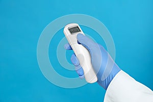 Doctor holding non contact infrared thermometer on blue background, closeup. Measuring temperature