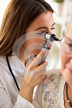 Doctor holding otoscope and examining ear of senior woman