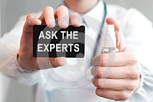 Doctor holding a paper card with text ASK THE EXPERTS and the medicine bottle, medical concept