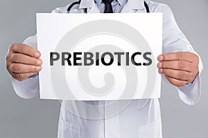 Doctor holding paper with word PREBIOTICS on light grey background, closeup photo