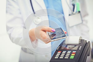 Doctor is holding payment terminal in hands. Paying for health care. Doctor