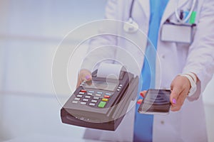 Doctor is holding payment terminal in hands. Paying for health care. Doctor