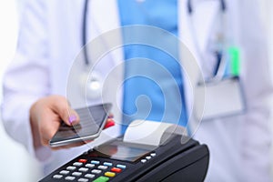 Doctor is holding payment terminal in hands. Paying for health care. Doctor