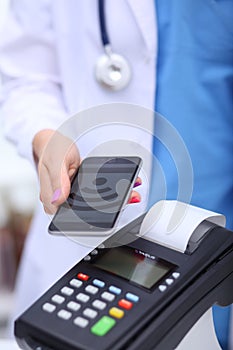 Doctor is holding payment terminal in hands. Paying for health care. Doctor