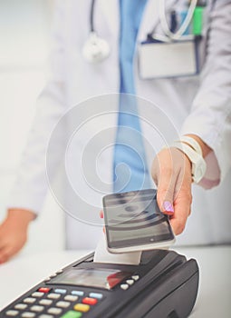 Doctor is holding payment terminal in hands. Paying for health care. Doctor