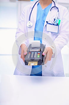 Doctor is holding payment terminal in hands. Paying for health care. Doctor