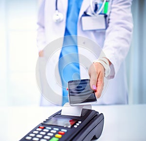 Doctor is holding payment terminal in hands. Paying for health care. Doctor