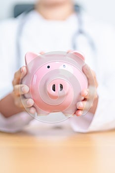 Doctor holding piggy bank and putting coin. and Healthcare cost, Money Saving, Health Insurance, Medical, Donation and Financial