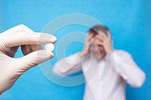 Doctor holding a pill for headache against the background of a man who has a headache, concept pills for headache, painkillers