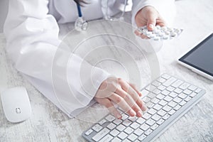 Doctor holding pills and typing in keyboard. Medicine