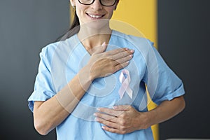 Doctor holding pink ribbon in hand near chest in clinic close-up