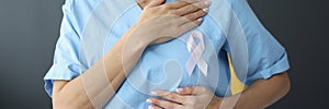 Doctor holding pink ribbon in hand near chest in clinic close-up