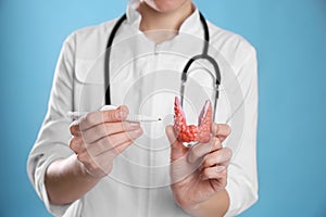 Doctor holding plastic model of afflicted thyroid on light blue background, closeup