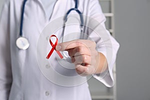 Doctor holding red awareness ribbon indoors, closeup. World AIDS disease day