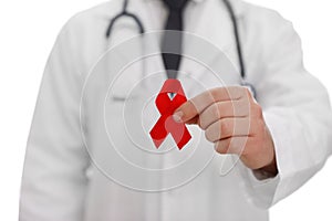 Doctor holding red ribbon on blurred background, closeup. AIDS awareness month