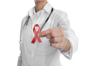 Doctor holding red ribbon on white background, closeup. AIDS awareness month
