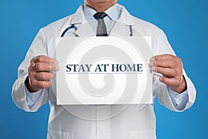 Doctor holding sign with text STAY AT HOME on background, closeup. Quarantine during coronavirus outbreak