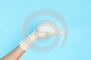 Doctor holding silicone implant for breast augmentation on color background, space for text