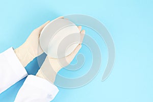 Doctor holding silicone implant for breast augmentation on color background, top view with space for text.