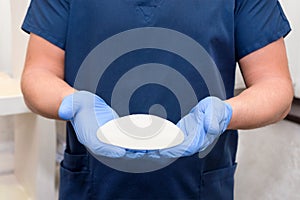 Doctor holding silicone implant for breast augmentation, space for text. Plastic surgeon hands holding silicon breast implants.