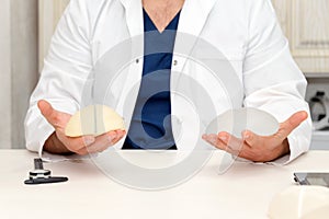 Doctor holding silicone implant for breast augmentation, space for text. Plastic surgeon hands holding silicon breast implants.