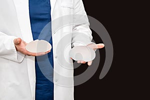 Doctor holding silicone implant for breast augmentation, space for text. Plastic surgeon hands holding silicon breast implants.