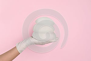 Doctor holding silicone implants for breast augmentation on color background, space for text.