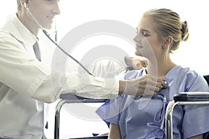 Doctor holding stethoscope for doing a physical examination of the young beautiful patient who setting on a wheelchair in medical