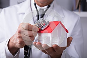 Doctor Holding Stethoscope On House Model