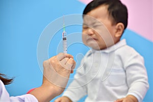 Doctor holding syringe with vaccine for Asian baby