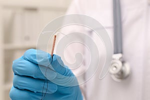 Doctor holding T-shaped intrauterine birth control device on blurred background, closeup. Space for text