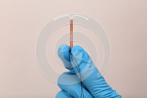 Doctor holding T-shaped intrauterine birth control device on grey background, closeup