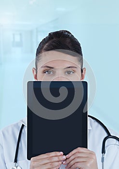 Doctor holding tablet over face in blue corridor