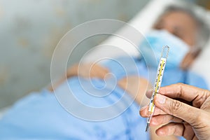 Doctor holding thermometer to measures asian senior or elderly old lady woman patient wearing a face mask have a fever in hospital