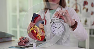 Doctor holds alarm clock near scientific heart model