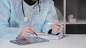 Doctor holds an electronic thermometer in his hand and works with a stylus on a tablet recording the results of
