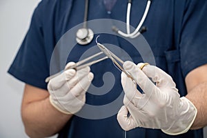 Doctor holds, in hand with disposable glove, forceps and needle holder and suture thread