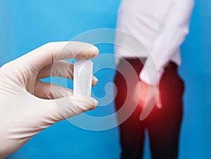 A doctor holds a healing suppository from problems with the rectum and hemorrhoids, the man holds on to the anus of the problem photo