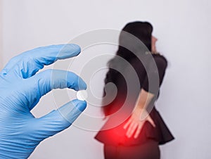 The doctor holds a pill for back pain, in the background a girl who has a back hernia and osteochondrosis, medicament photo