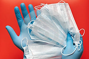 Doctor holds respiratory surgical face mask in hands blue medical gloves on red background
