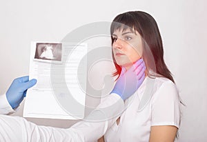 The doctor holds the results of an ultrasound examination of the throat against the background of a caucasian female patient who