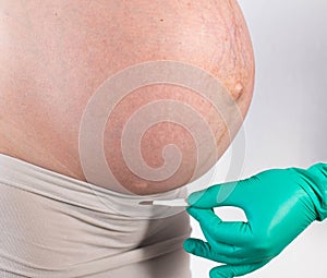 The doctor holds a scalpel against the background of the belly of a pregnant girl. The concept of caesarean section in pregnant