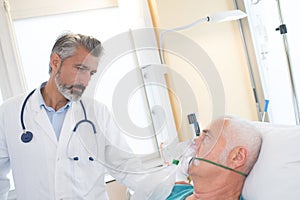 Doctor at hospital bedroom with sick patient lying in bed