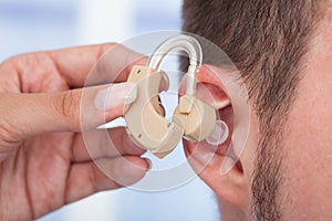 Doctor inserting hearing aid in man's ear